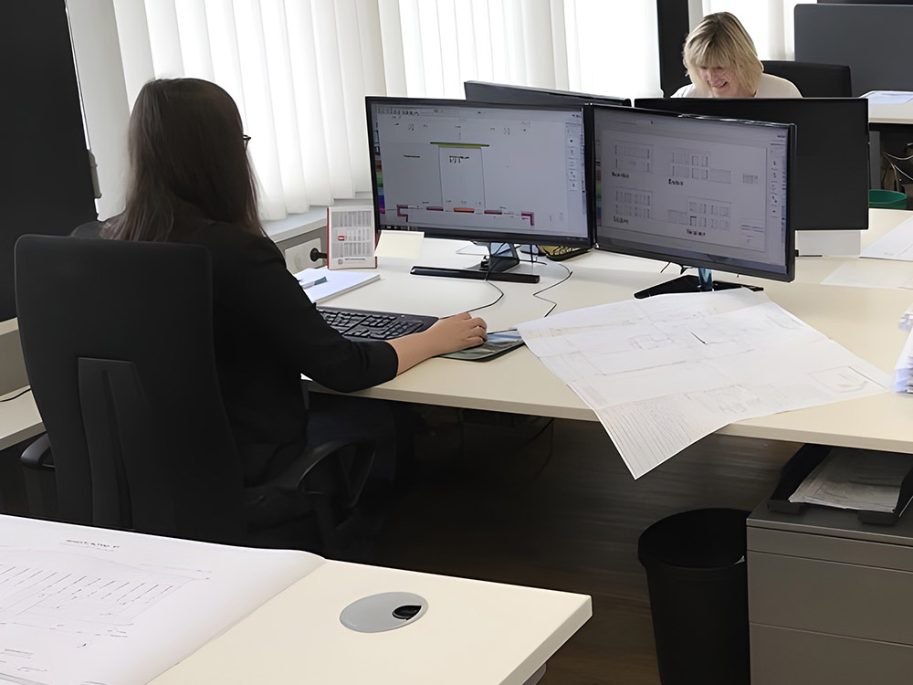 Architekturplanung am Bildschirm – präzises Arbeiten mit CAD-Software im BAUATELIER Grunwald Zwei Mitarbeiterinnen arbeiten mit technischen Bauplänen an großen Monitoren in einem modernen Büro